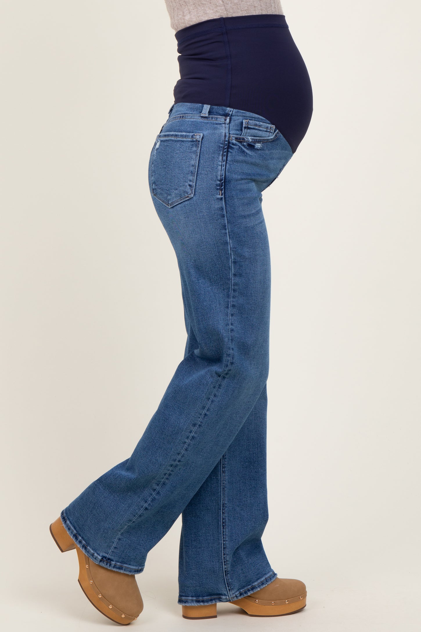 woman wearing dark blue maternity jeans with a supportive belly panel and flared legs, showcasing her baby bump