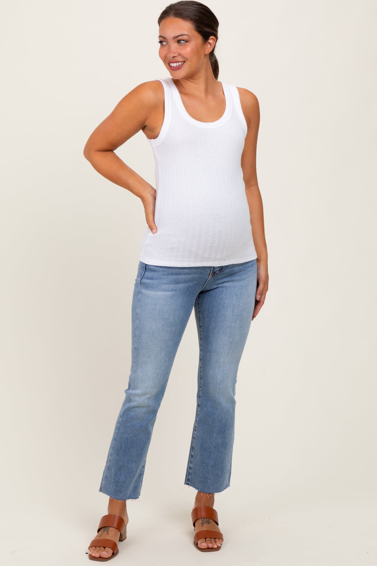 woman wearing a white ribbed maternity tank top and light blue flared jeans, showing her baby bump