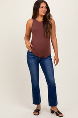 woman wearing a brown maternity tank top and blue jeans, showing her baby bump while posing confidently