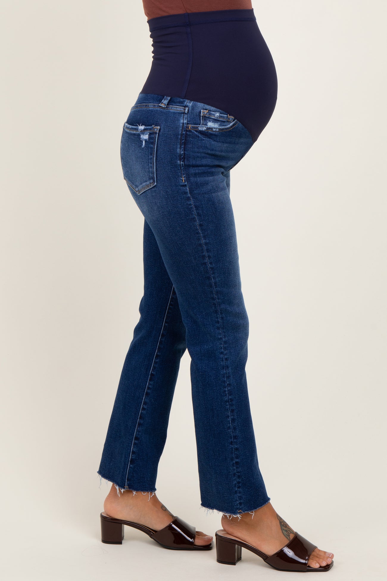 woman wearing dark blue maternity jeans with a frayed hemline and a visible baby bump
