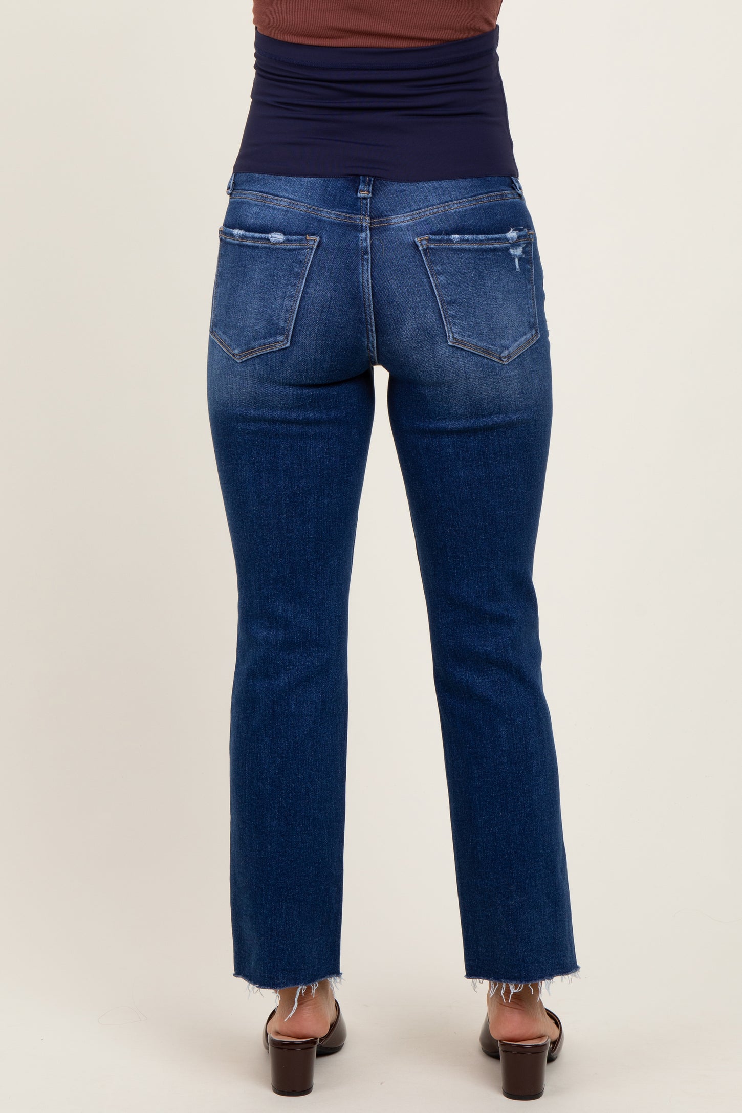 woman wearing dark wash distressed maternity jeans with a flared leg and frayed hem, seen from the back