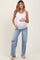 woman wearing a white ribbed maternity tank top and distressed light wash maternity jeans, showing her baby bump