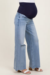 woman wearing light blue distressed wide-leg maternity jeans with a navy belly band, showcasing her baby bump