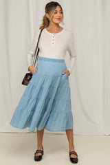 woman wearing a light gray long sleeve maternity top and a blue tiered maxi skirt with pockets