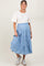 woman wearing a cream short sleeve top and a light blue tiered maternity maxi skirt, holding the skirt while smiling