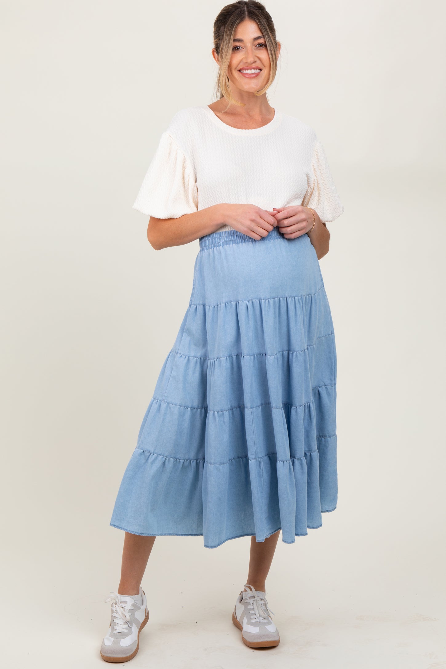 woman wearing a light blue tiered maternity skirt and a white short sleeve top, standing with hands on her hips