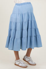 woman wearing a light blue tiered denim maternity skirt with an elastic waist and white sneakers