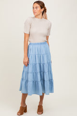 woman wearing a ribbed beige short sleeve top and a tiered light blue denim midi skirt with brown heeled sandals