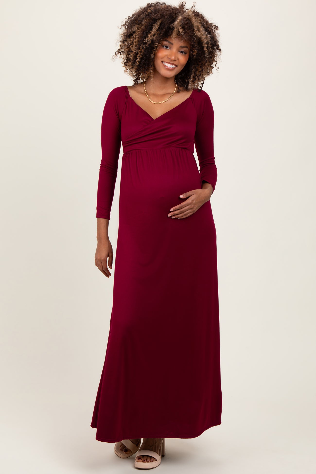 woman wearing a burgundy long sleeve maternity maxi dress and holding her baby bump