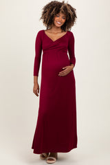 woman wearing a burgundy long sleeve maternity maxi dress and holding her baby bump