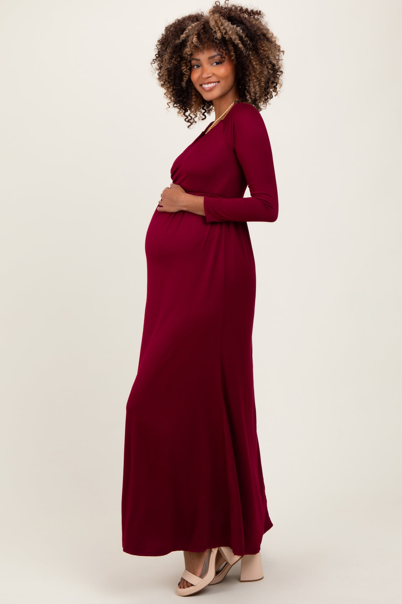 woman wearing a burgundy long sleeve maternity dress, showcasing her baby bump while standing in profile