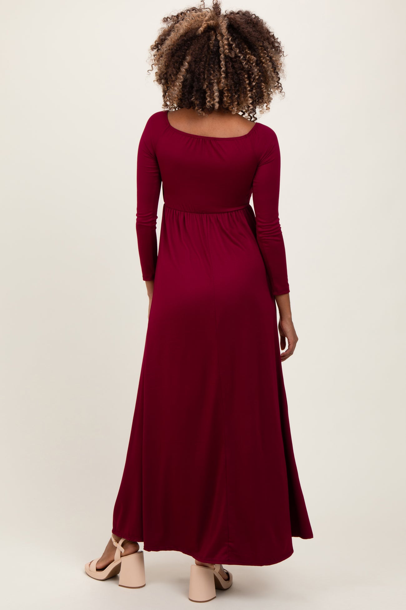 woman wearing a long burgundy maternity dress with three-quarter sleeves and a flowing skirt, showing her baby bump