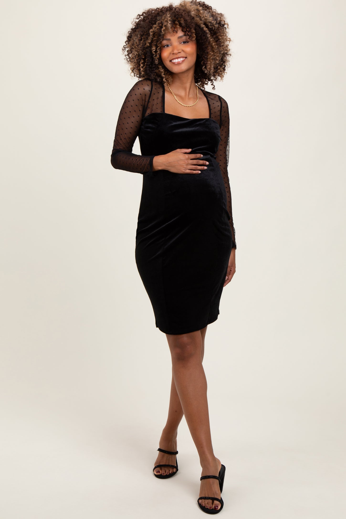 woman wearing a black maternity dress with dotted long sleeves and a fitted silhouette, showing her baby bump
