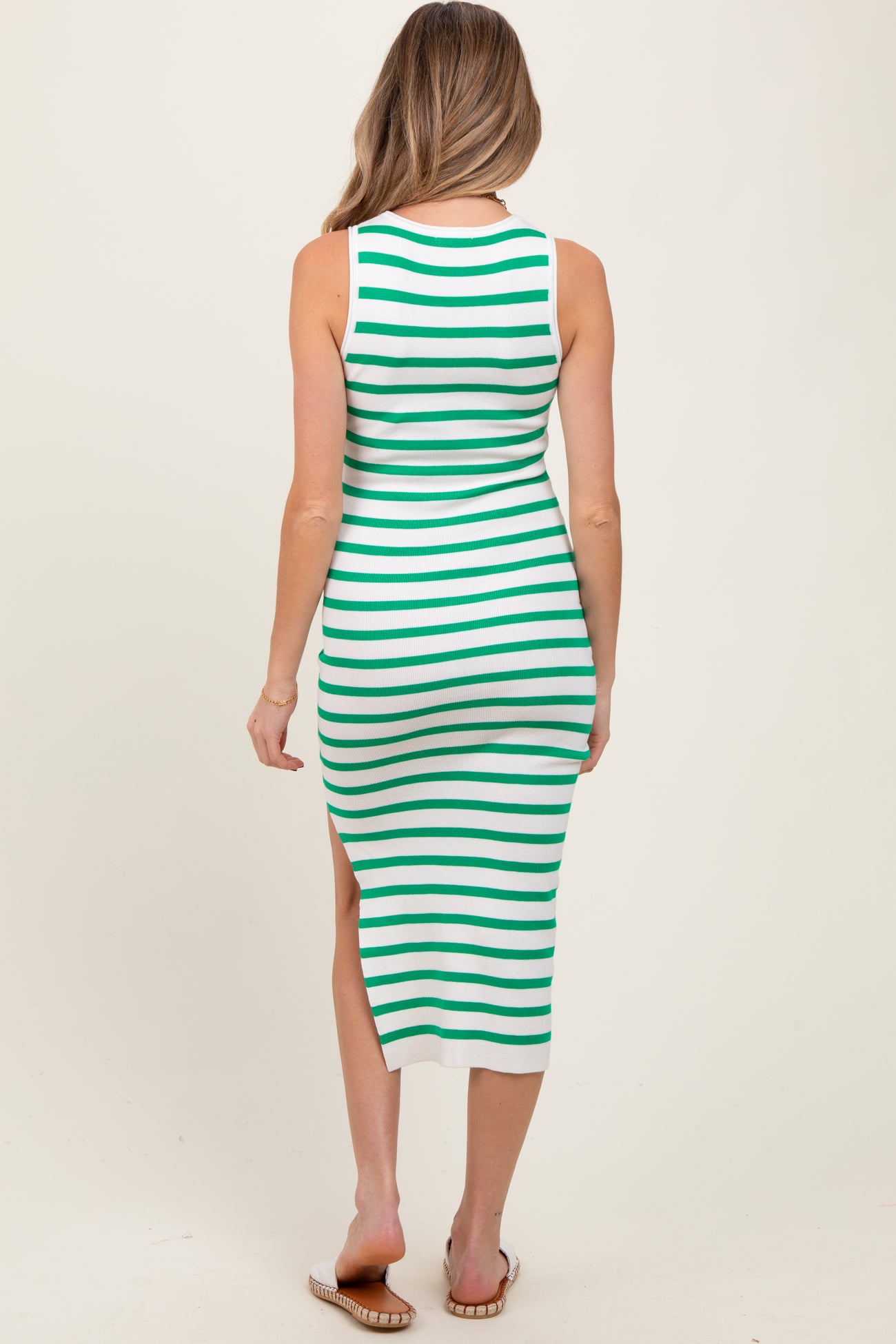 maternity wear of a woman wearing a green and white striped sleeveless dress with a thigh slit and form-fitting style