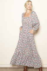 woman wearing a floral maxi dress with long puff sleeves and pockets, smiling against a plain background