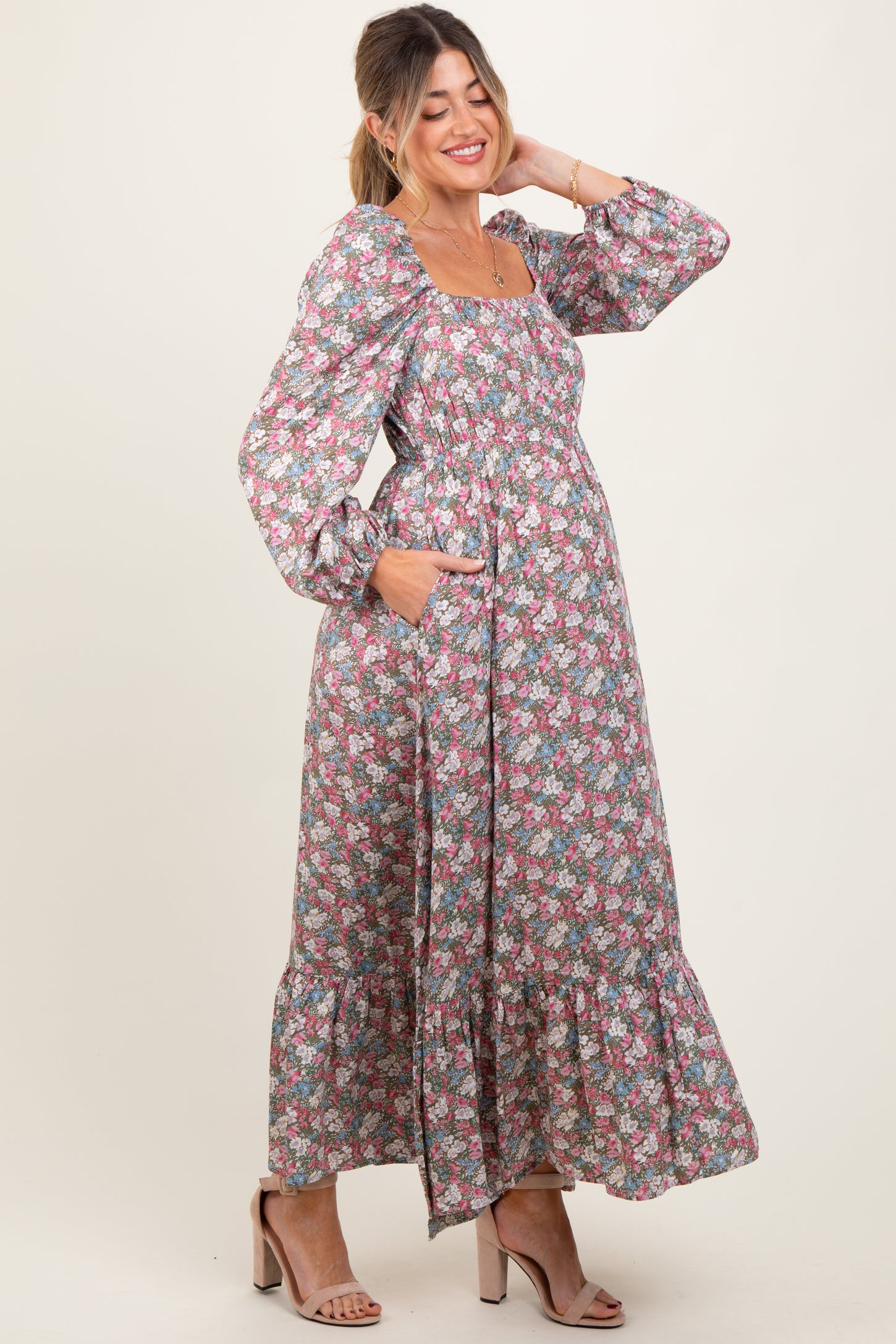 woman wearing a floral maternity maxi dress with long sleeves and pockets, smiling and showing her baby bump