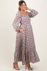 woman wearing a floral maternity maxi dress with long sleeves and pockets, smiling and showing her baby bump