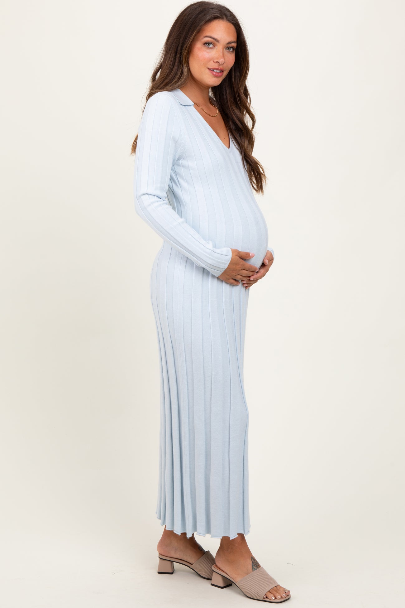 woman wearing a light blue ribbed maternity dress with a v-neck and long sleeves, holding her baby bump