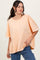 woman wearing an oversized peach short sleeve top with a round neckline and relaxed fit paired with blue jeans