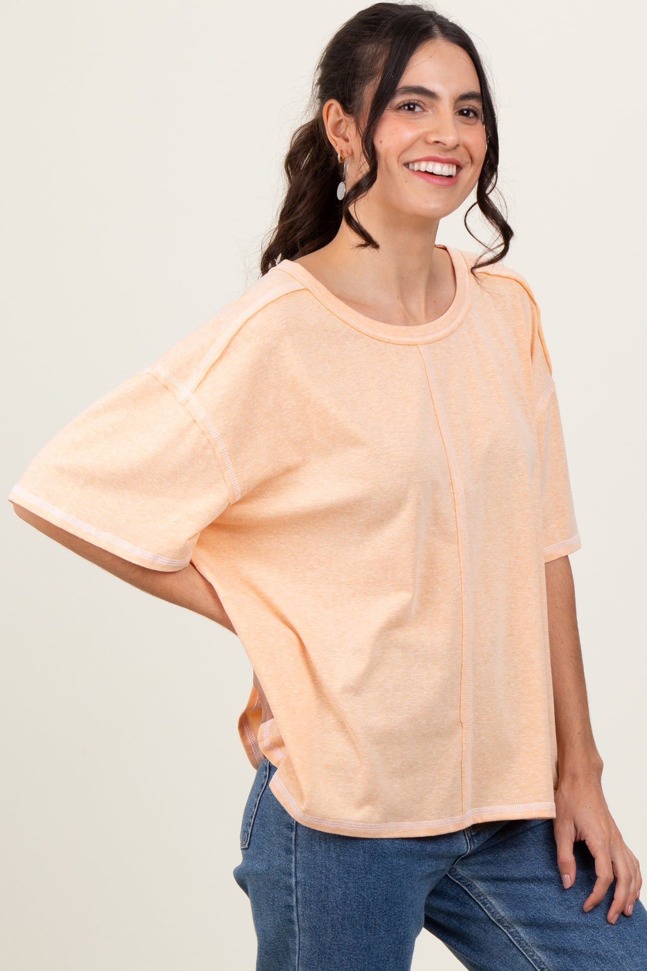 woman wearing a light peach oversized t-shirt with short sleeves and a relaxed fit, smiling and standing sideways