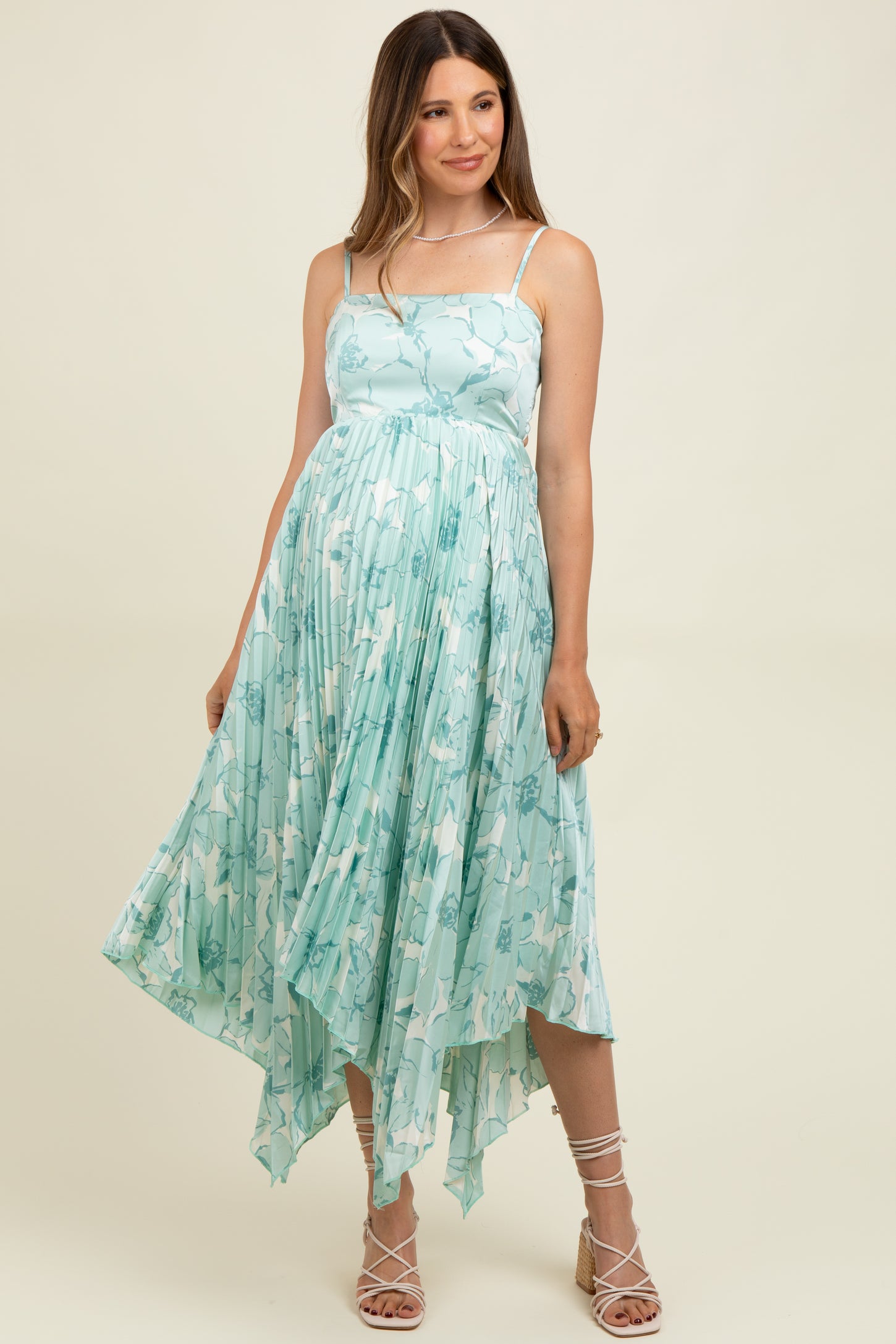 woman wearing a light blue floral print maternity dress with a high-low hem and spaghetti straps, showing her baby bump