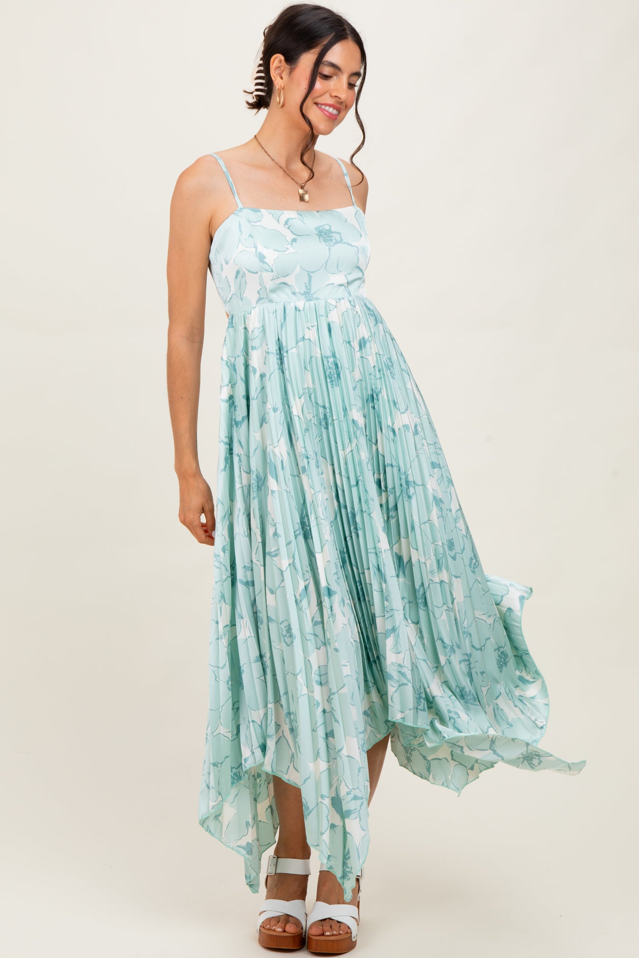 woman wearing a light green floral maxi dress with a high-low hem and spaghetti straps