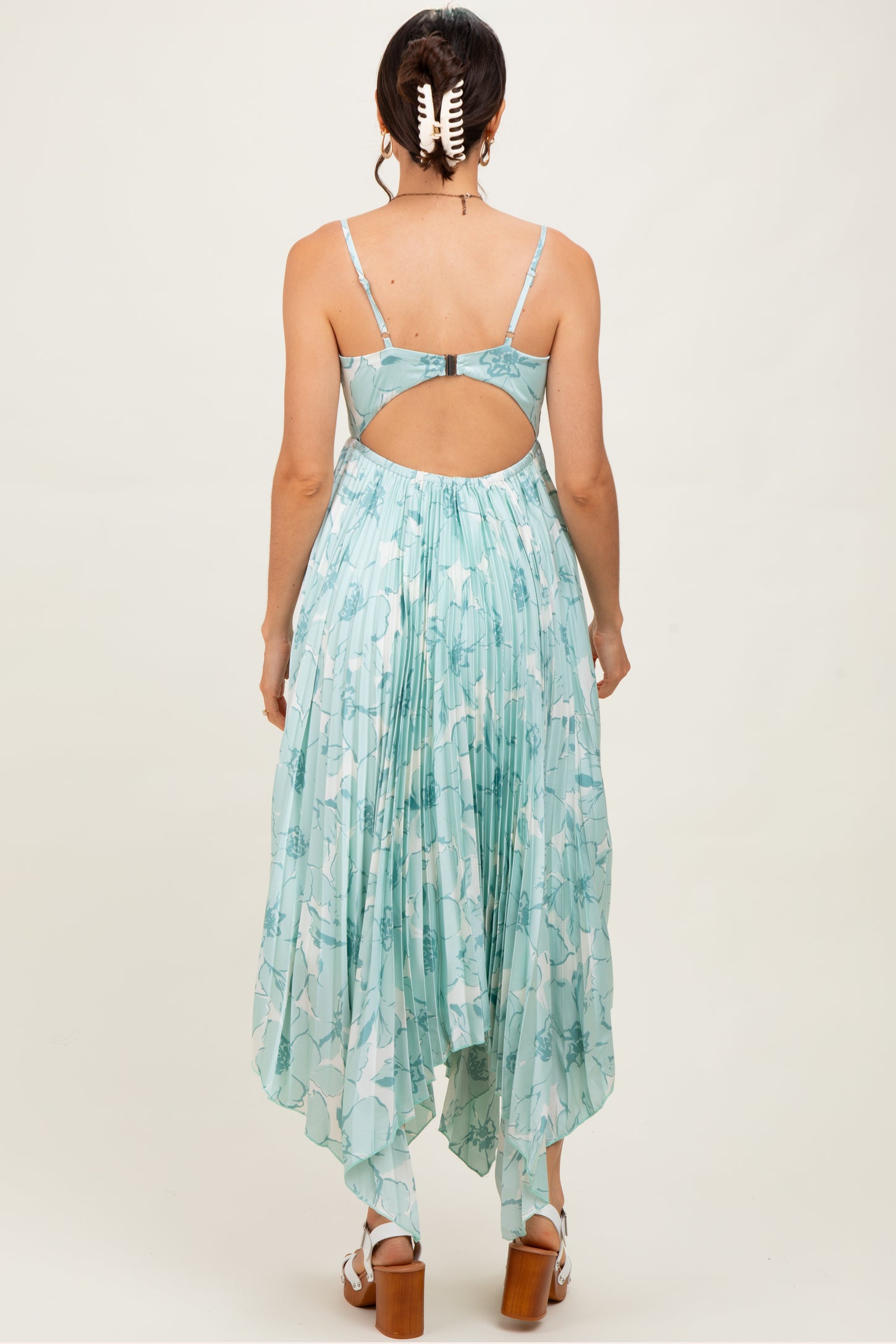 woman wearing a light blue floral print maxi dress with a cutout back and pleated design, standing with her back to the camera