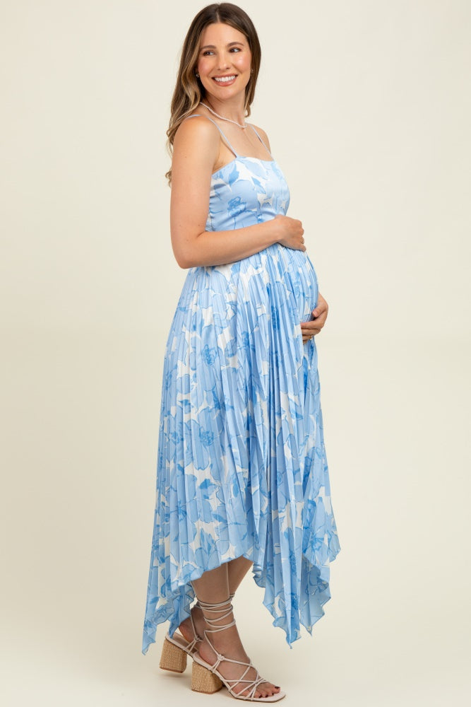 woman wearing a light blue maternity dress with a floral pattern, featuring a high-low hem and holding her baby bump