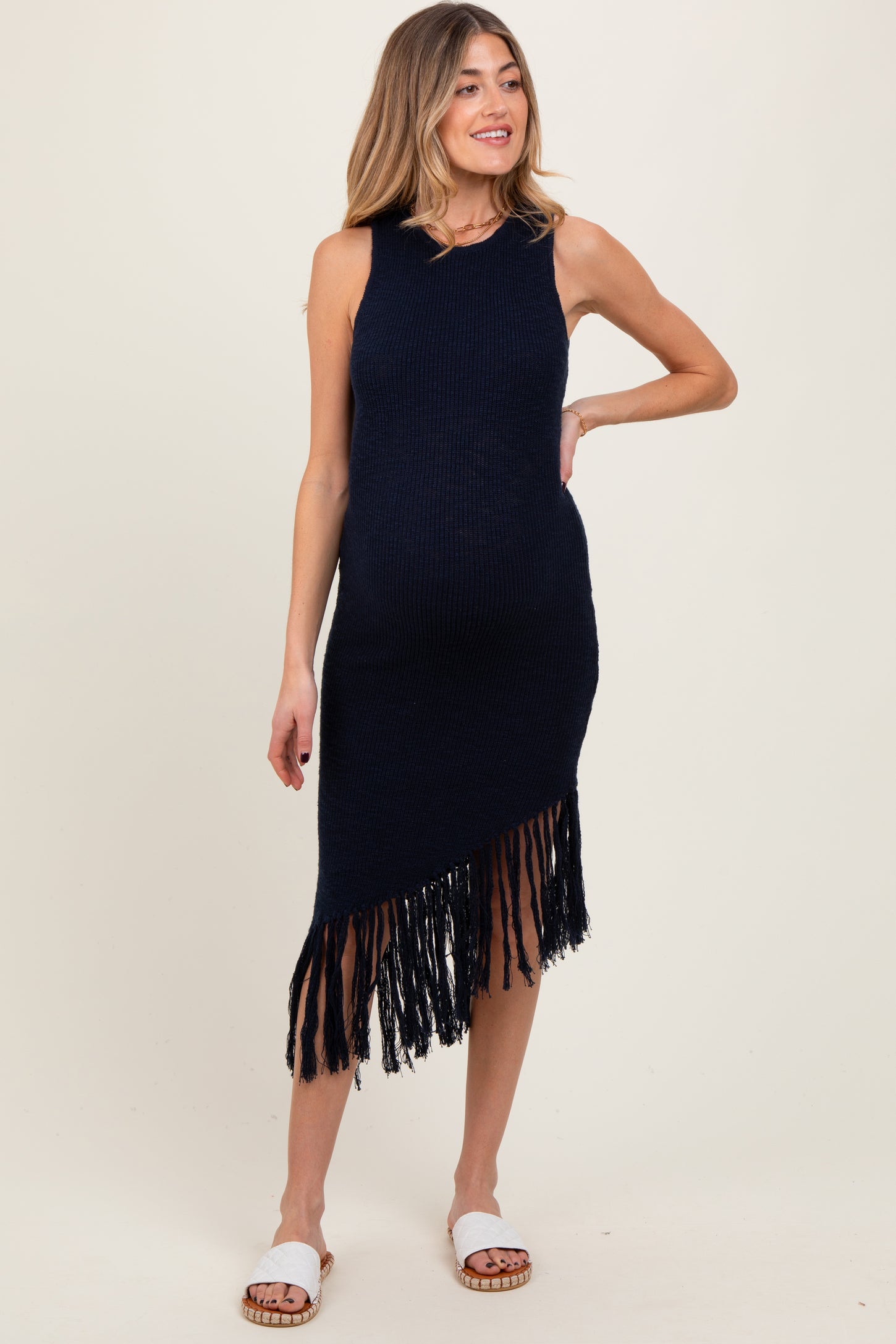 woman wearing a navy blue sleeveless knitted maternity dress with fringe detailing and a visible baby bump