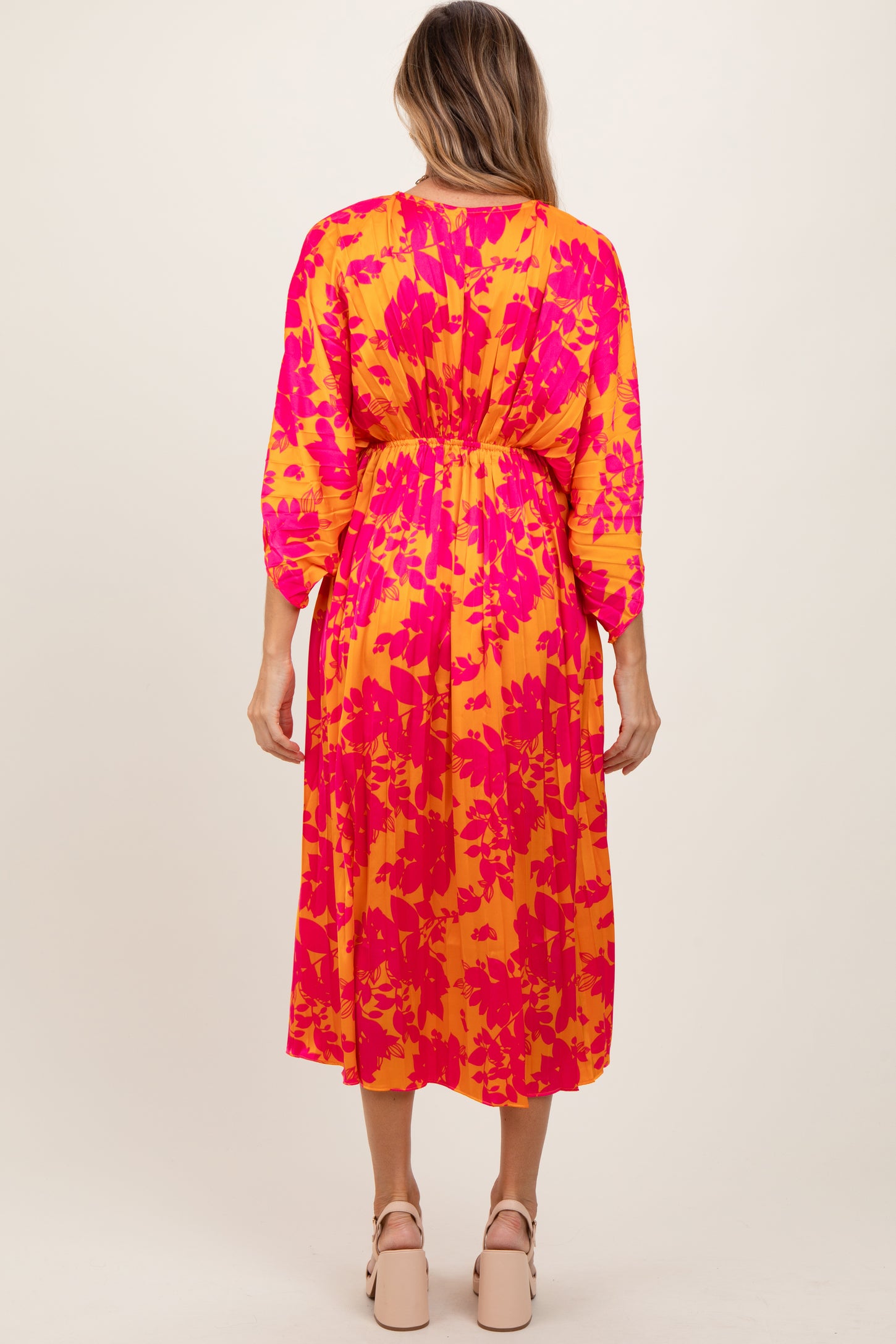 woman wearing a colorful floral midi dress with a cinched waist and three-quarter sleeves, viewed from the back