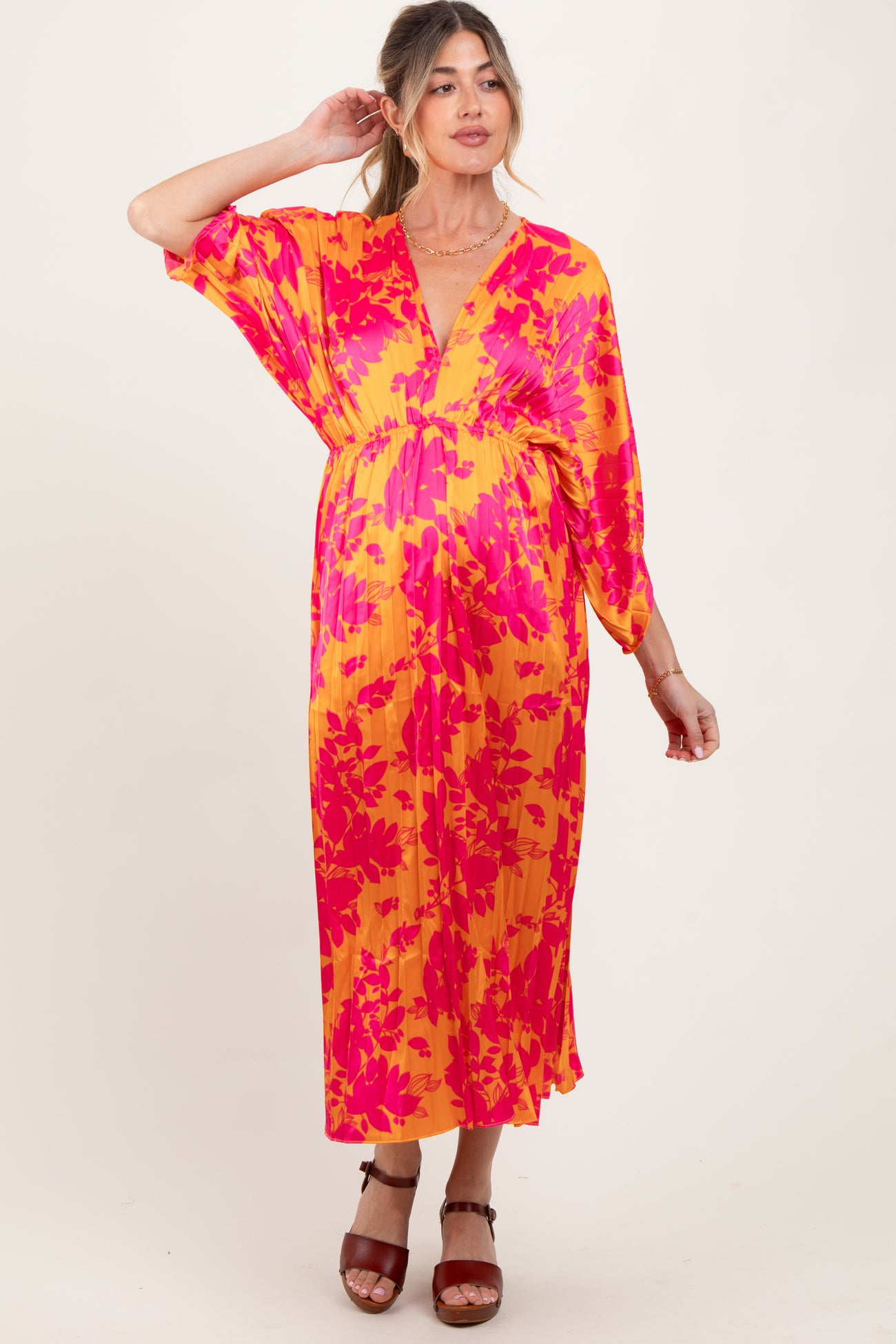 woman wearing a vibrant yellow and pink floral maternity dress with a deep v-neck and flowing sleeves, styled with brown heels