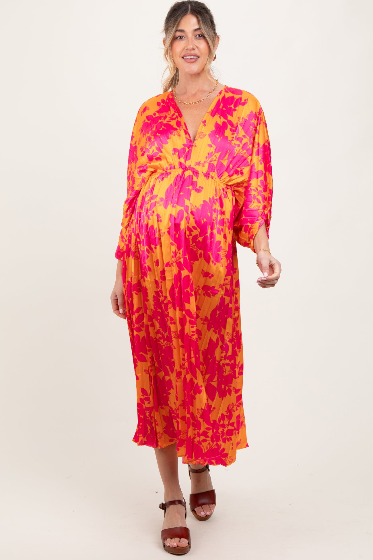 woman wearing a vibrant pink and orange patterned maternity dress with a v-neckline and three-quarter sleeves, displaying a baby bump