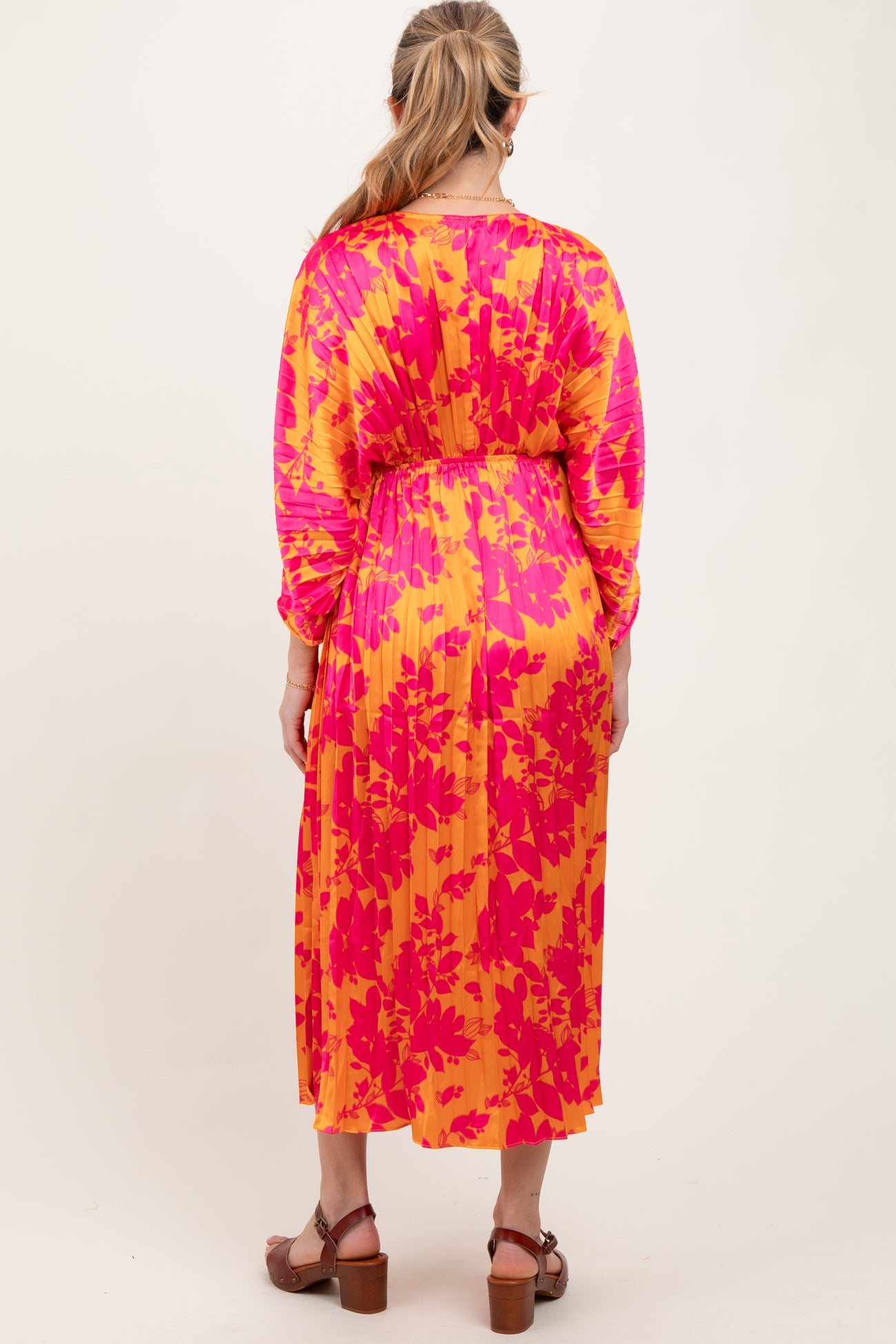 woman wearing a vibrant pink and yellow floral print maternity dress with long sleeves and a cinched waist, back view