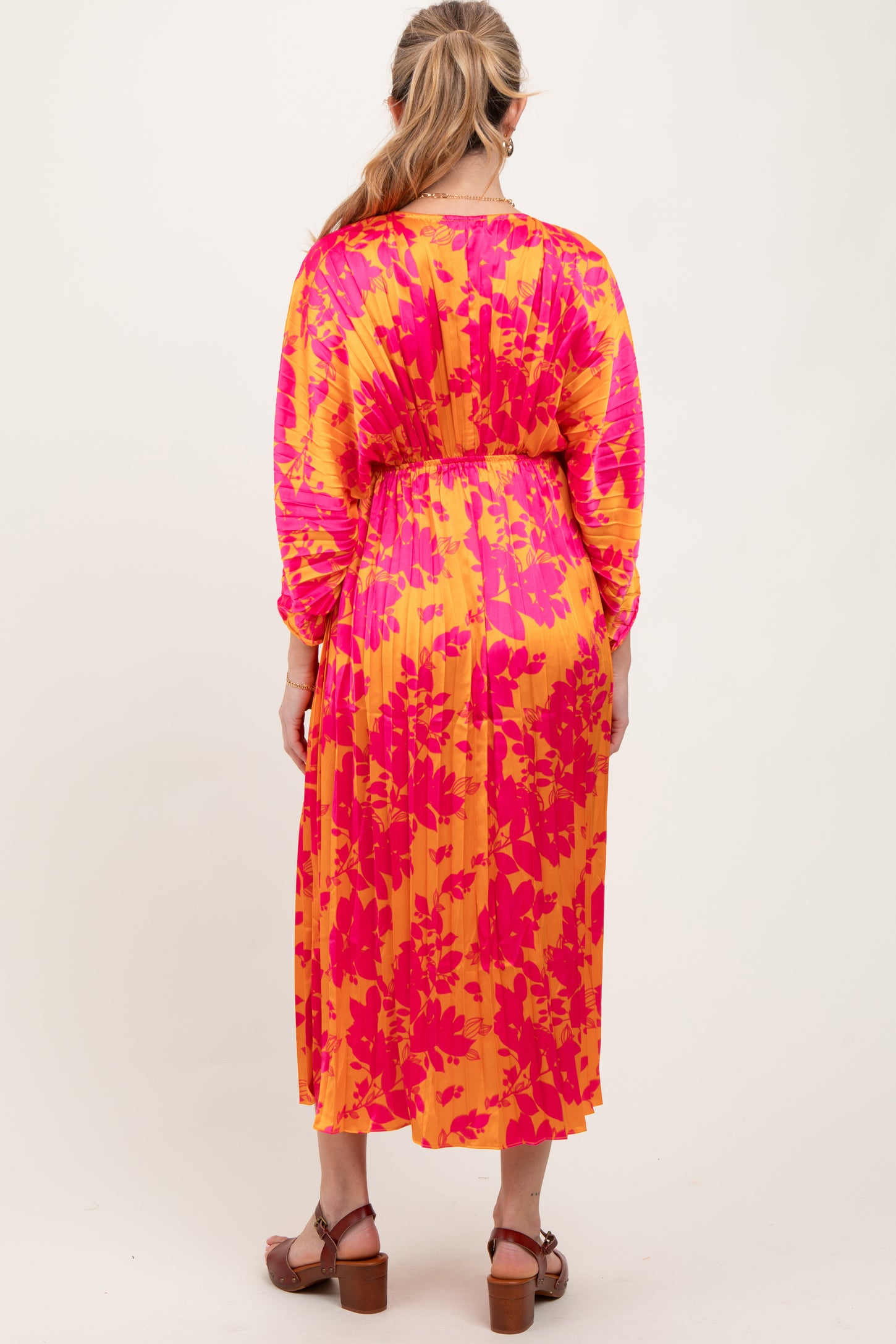 woman wearing a vibrant pink and yellow floral print maternity dress with long sleeves and a cinched waist, back view