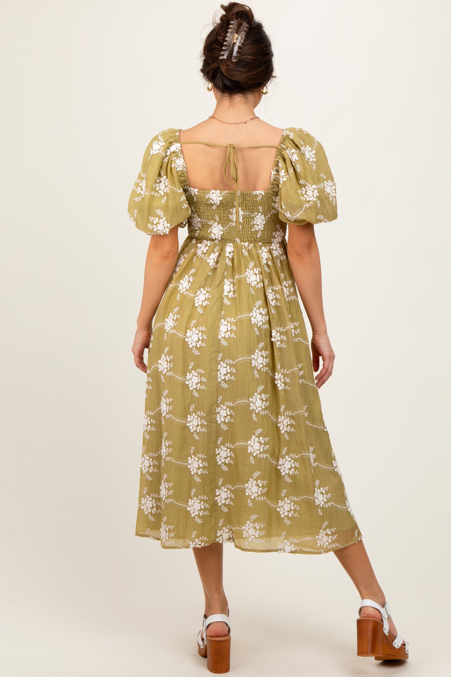 woman wearing a green floral midi dress with puff sleeves and a smocked back, standing with her back to the camera