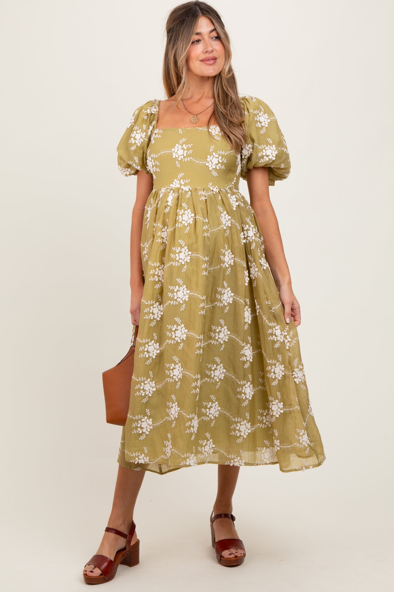 woman wearing a yellow floral maternity dress with puff sleeves and a square neckline, holding a brown bag