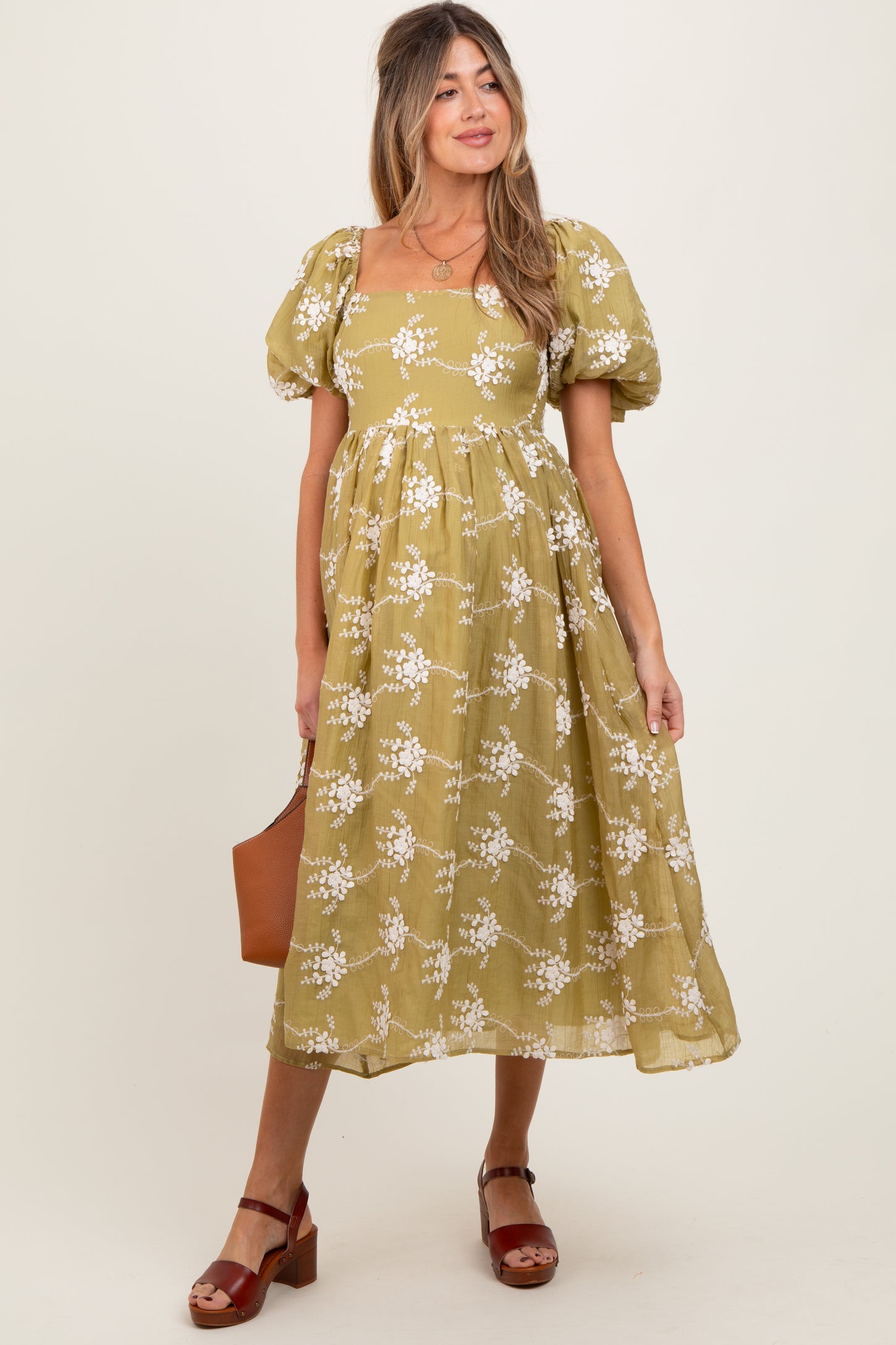 woman wearing a yellow floral maternity dress with puff sleeves and a square neckline, holding a brown bag