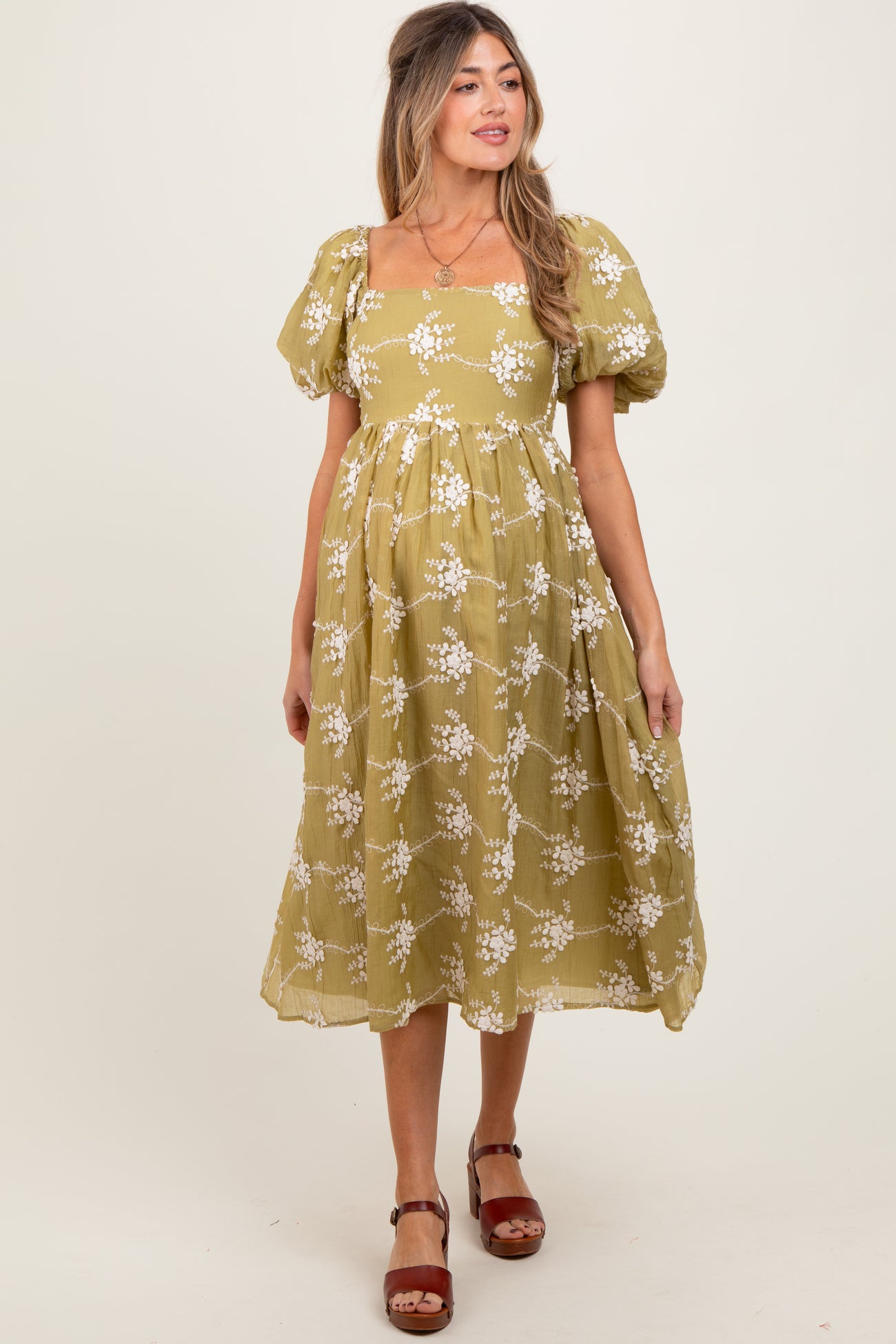 woman wearing a green maternity dress with floral print and puff sleeves, standing and smiling