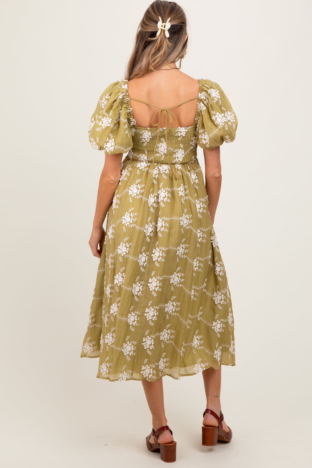 woman wearing a green maternity dress with puffed sleeves and floral print, showing the back view