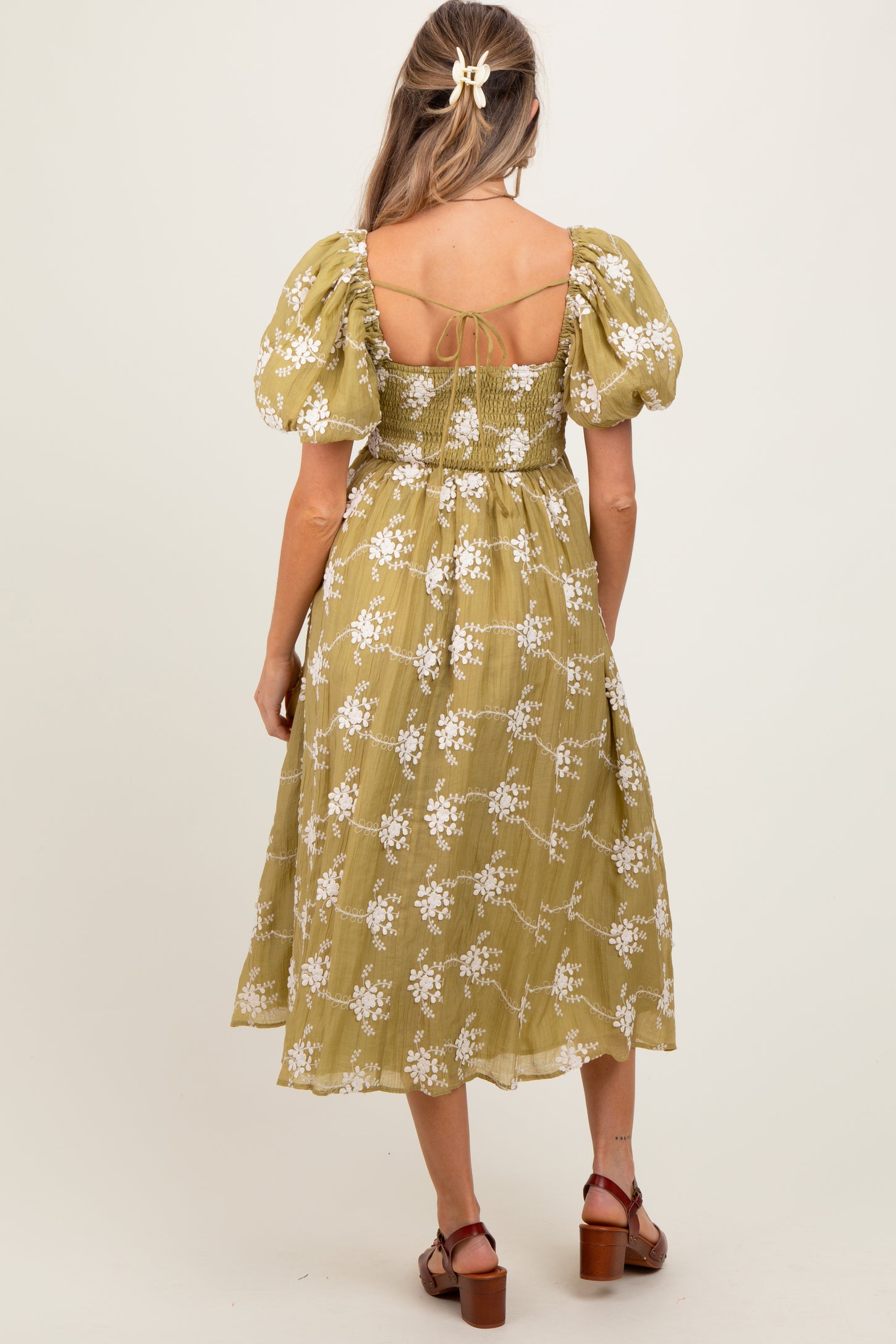 woman wearing a green maternity dress with puffed sleeves and floral print, showing the back view