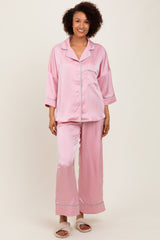 woman wearing a light pink satin pajama set with button-up top and wide-leg pants, standing and smiling
