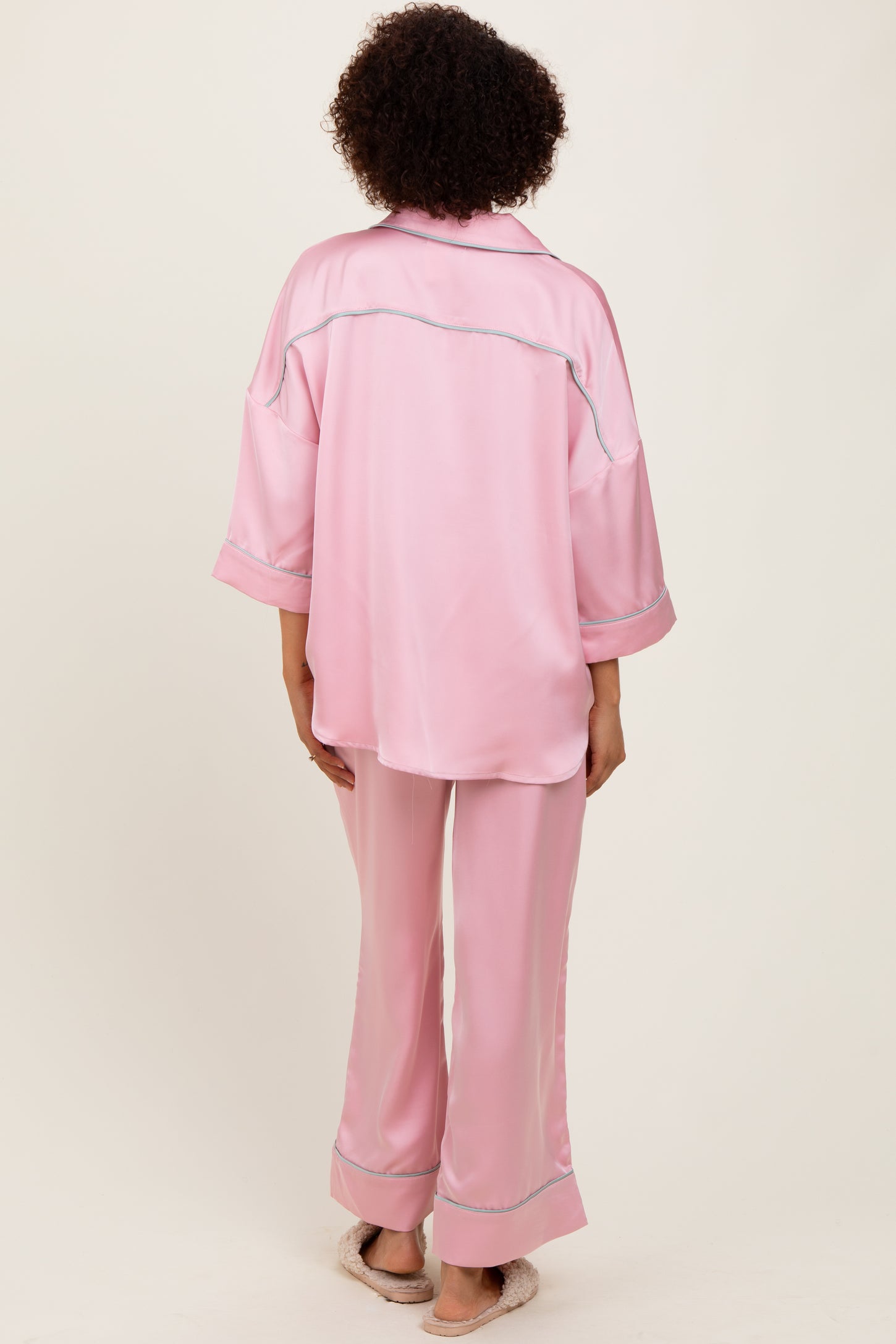 woman wearing a pink satin pajama set with a loose-fitting top and wide-leg pants, seen from the back