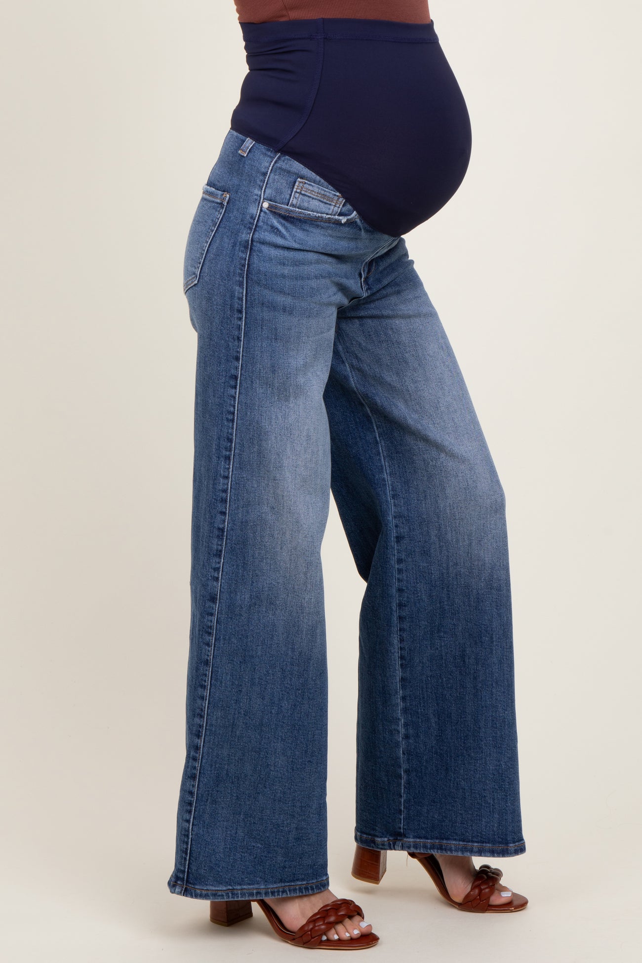 woman wearing a navy blue maternity top and wide-leg blue maternity jeans, showing her baby bump