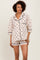 woman wearing a beige short sleeve pajama set with black bow print and trim, featuring shorts and a button-up top