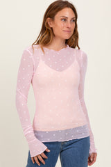 woman wearing a light pink long sleeve top with white heart print and ruffled neckline, styled with denim jeans