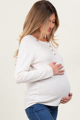 woman wearing a cream long sleeve maternity top with buttons, gently cradling her baby bump