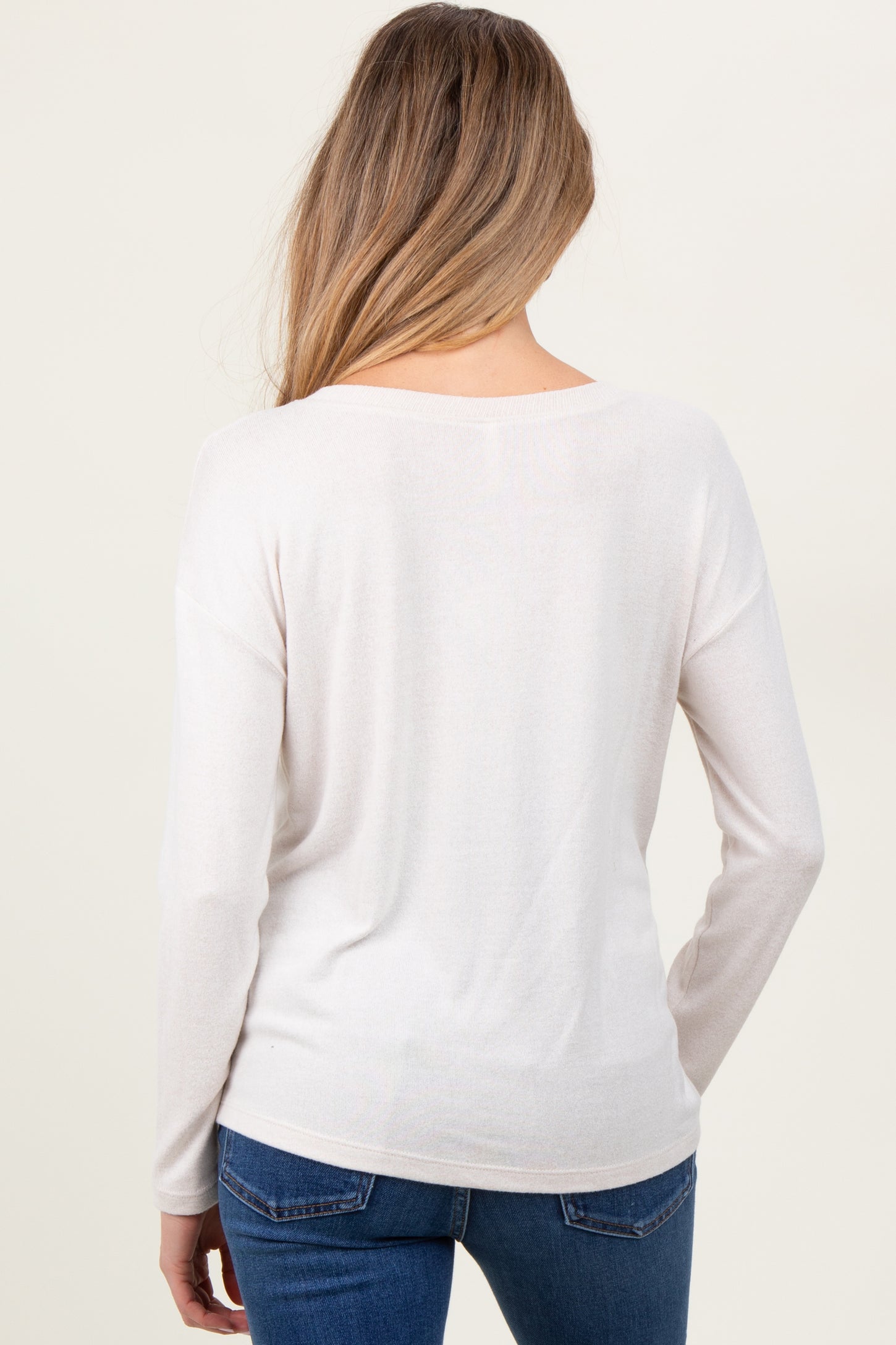 woman wearing a light beige long sleeve maternity sweater, viewed from the back, paired with blue jeans