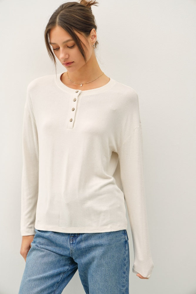 woman wearing a cream long sleeve henley shirt with button details and casual blue jeans