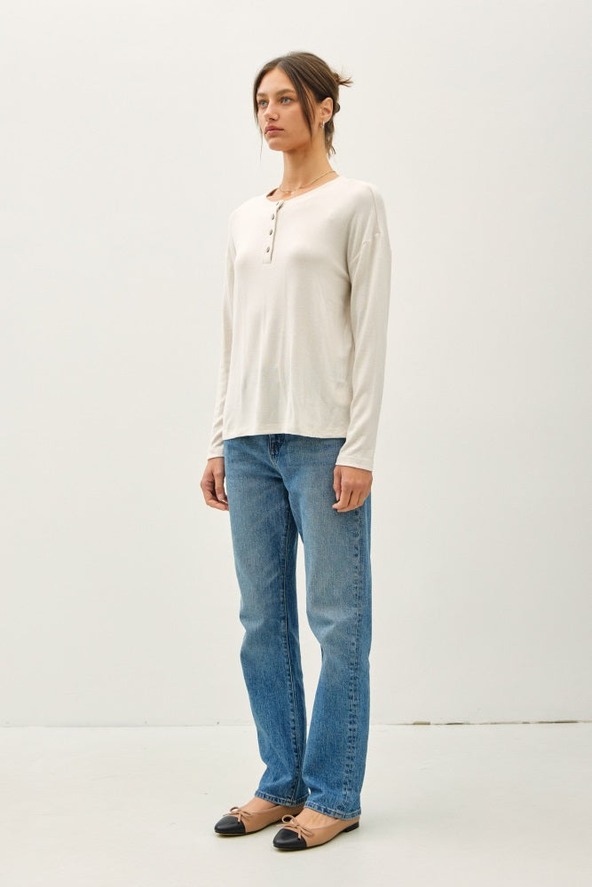 woman wearing a cream long sleeve henley top with buttons, paired with light blue straight-leg jeans and flat shoes
