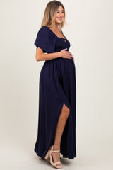 woman wearing a navy blue maternity maxi dress with a smocked bodice and side slit, holding her baby bump